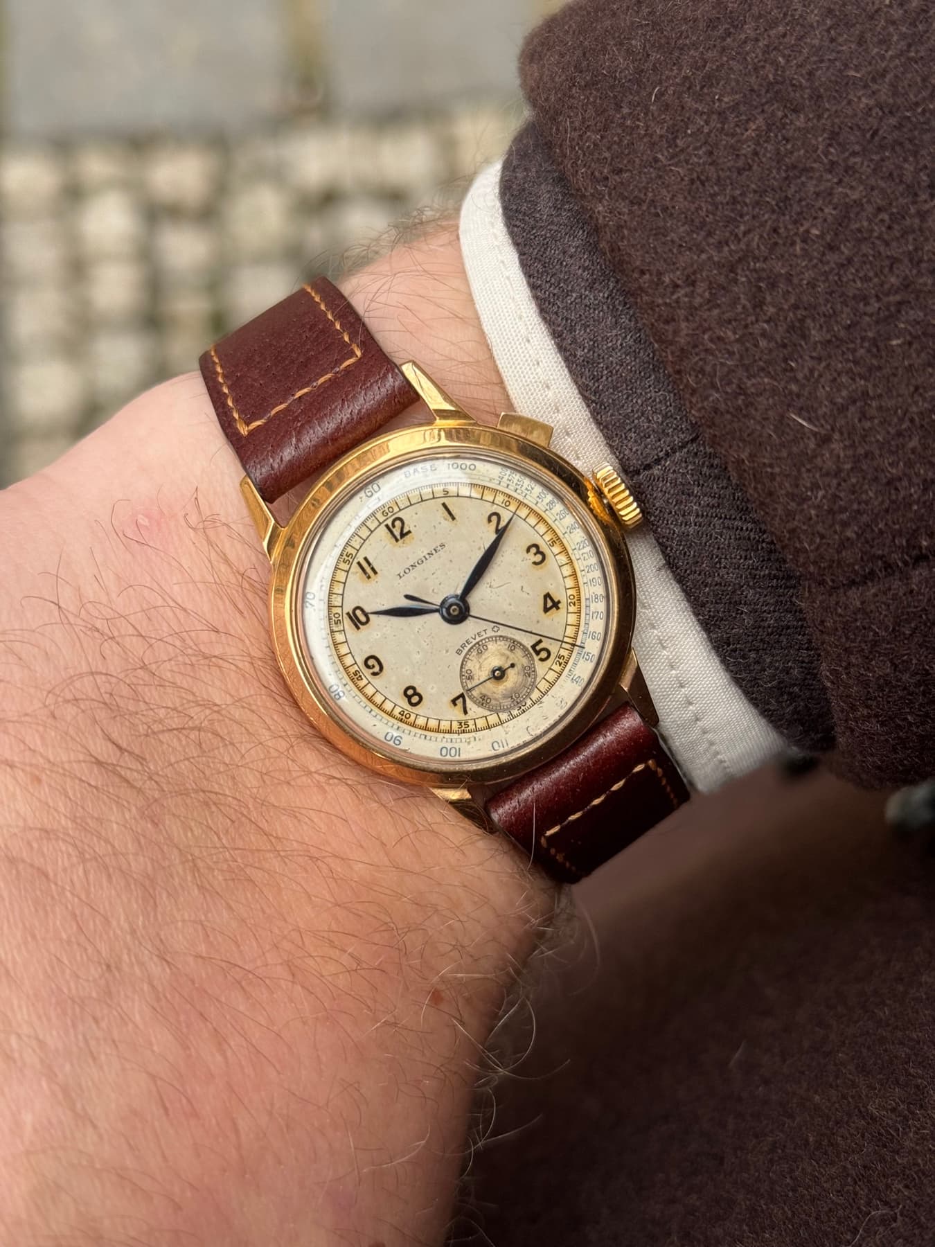 Vintage gold chronograph on a burgundy leather strap, worn on the wrist in Prague